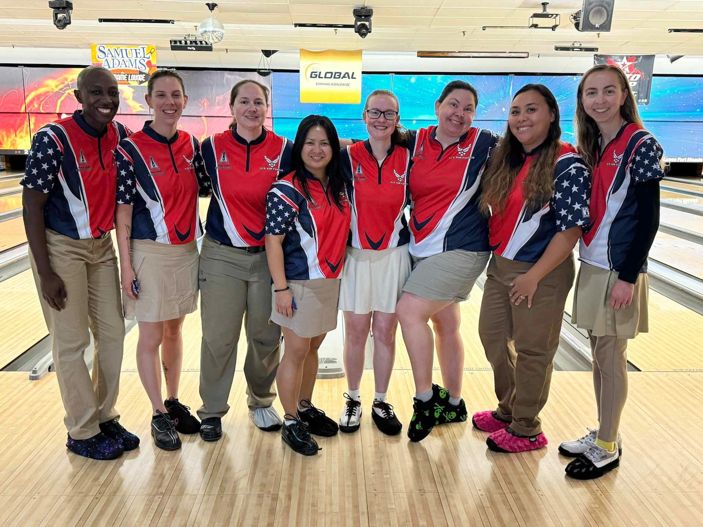 Female group photo of women wearing bowling uniforms at a bowling alley in front of bowling lanes