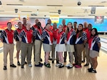 Group members in bowling uniforms pose for a photo at a bowling alley in front of bowling lanes