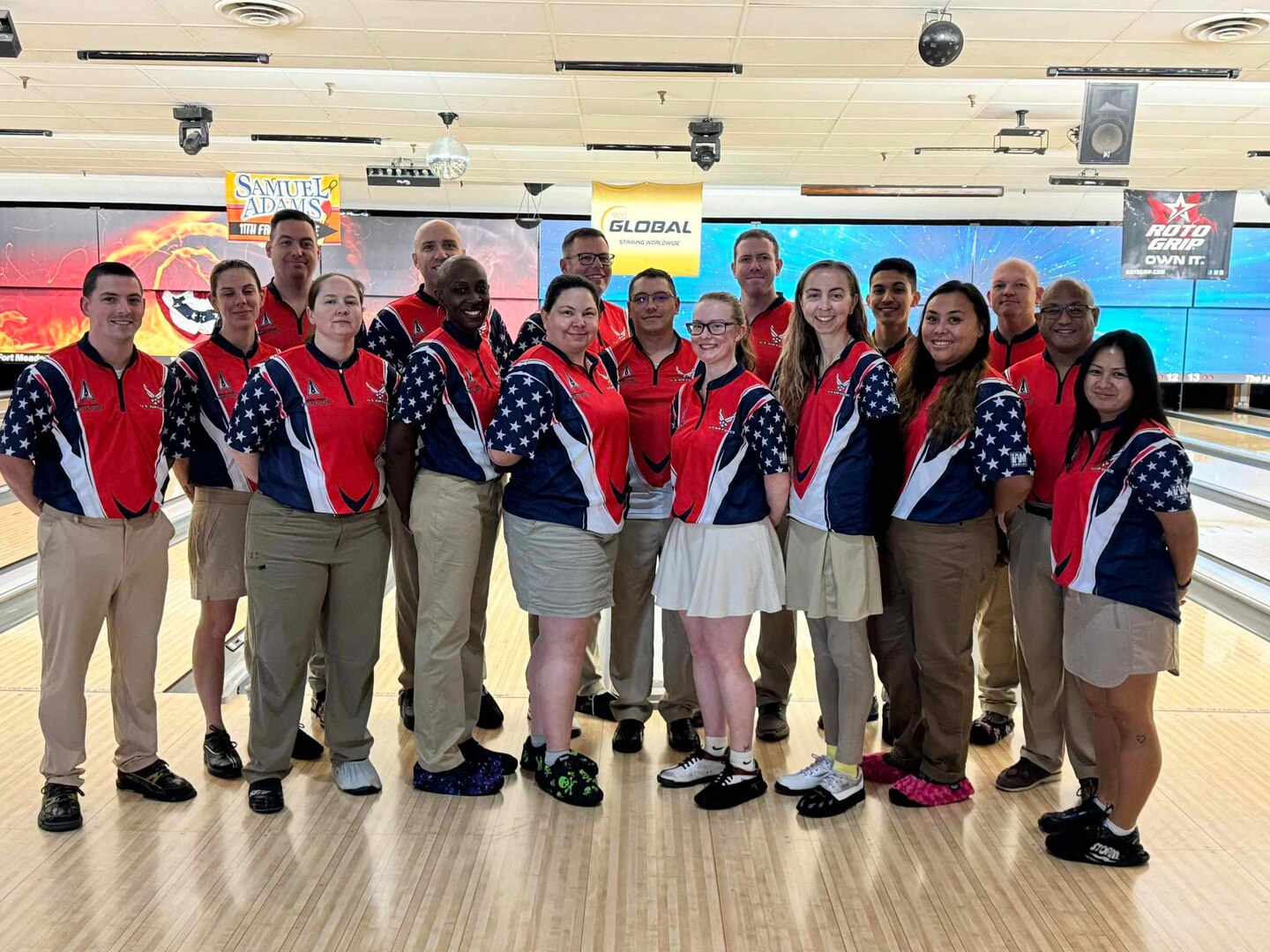 Group members in bowling uniforms pose for a photo at a bowling alley in front of bowling lanes