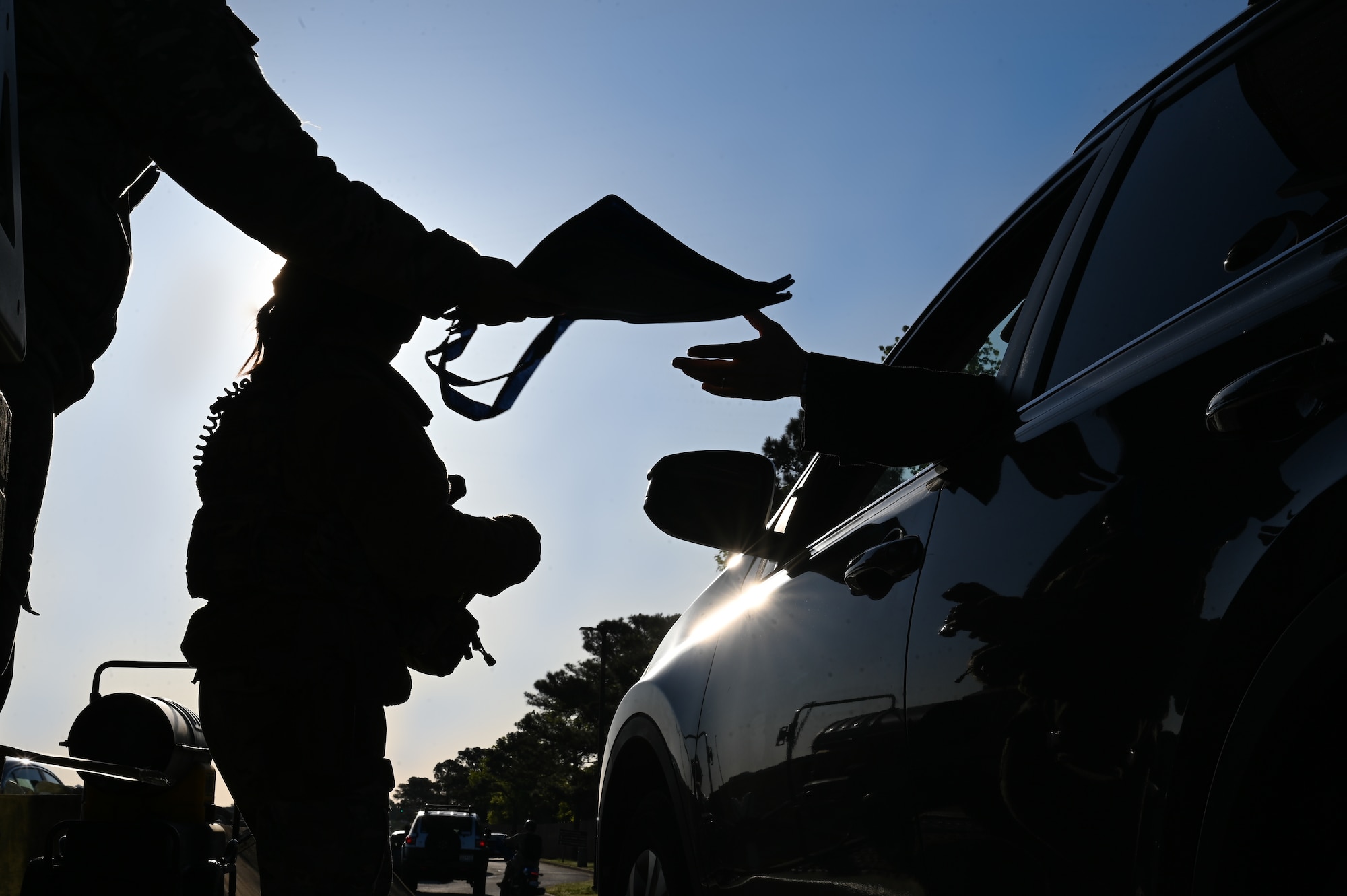 Silhouette photo of an Airman passing a reusable back to a person driving onto base.