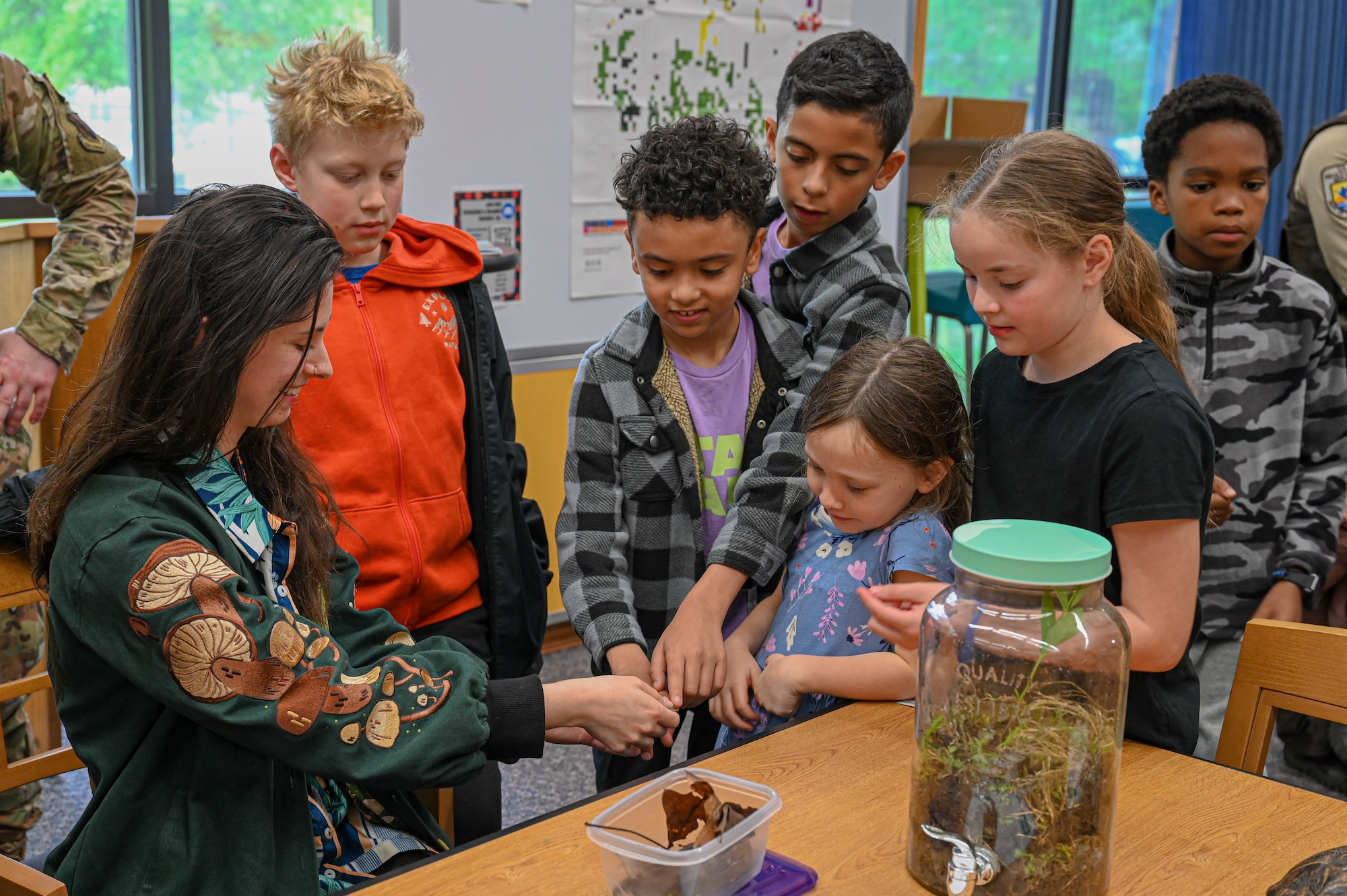 Photo of woman holding a worm snake with kids standing around, looking and touching.
