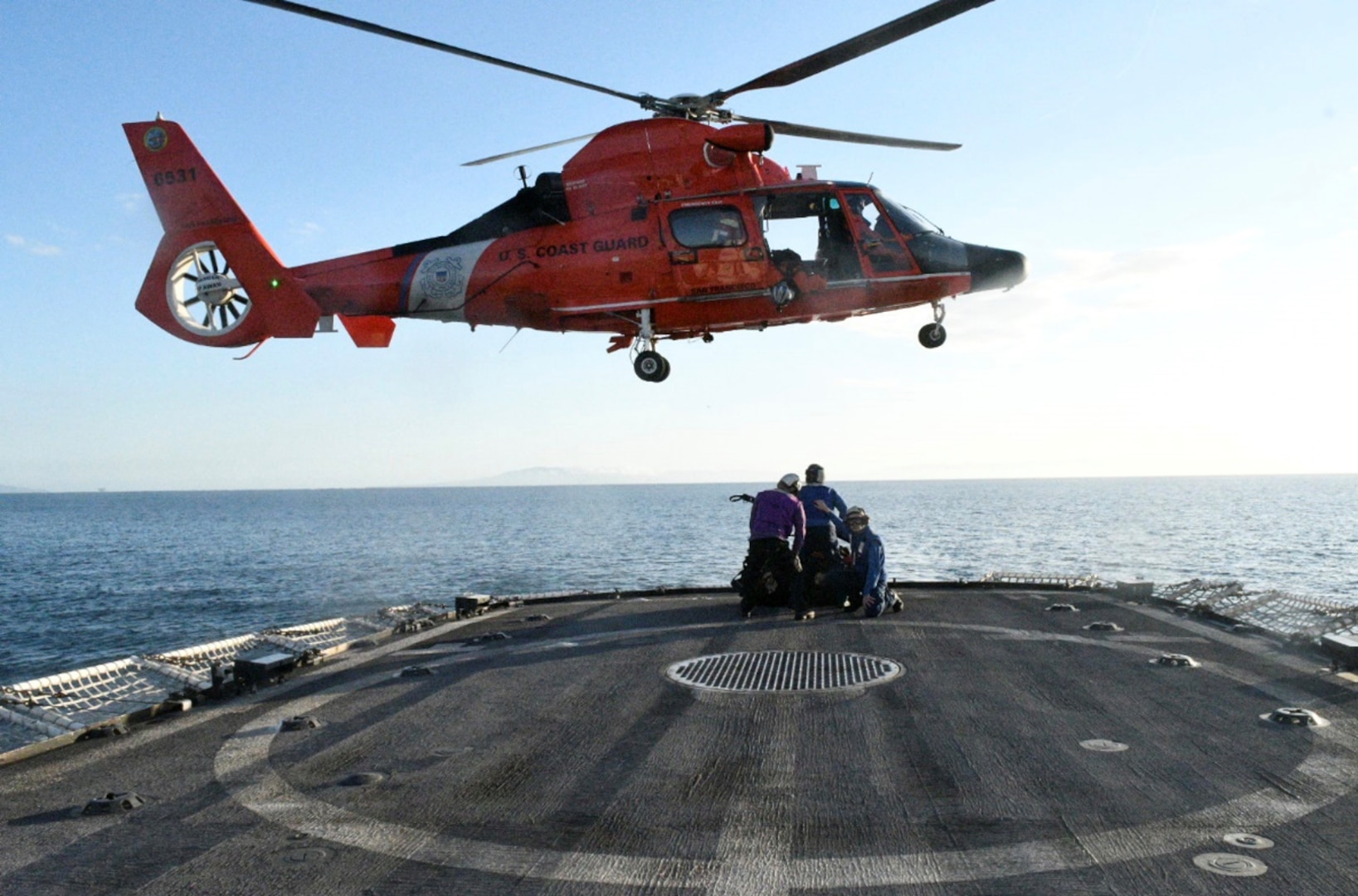 USCGC Active (WMEC 618) crewmembers assigned to the cutter’s hook-up team prepare to attach a load during a vertical replenishment (VERTREP) exercise off the coast of Southern California with an MH-65E helicopter aircrew from Forward Operation Base Point Mugu, California, Mar. 17, 2024. A VERTREP is a logistical operation to resupply ships at sea utilizing helicopters to transport supplies and equipment between ships. U.S. Coast Guard photo by Chief Petty Officer Shane Sexton.