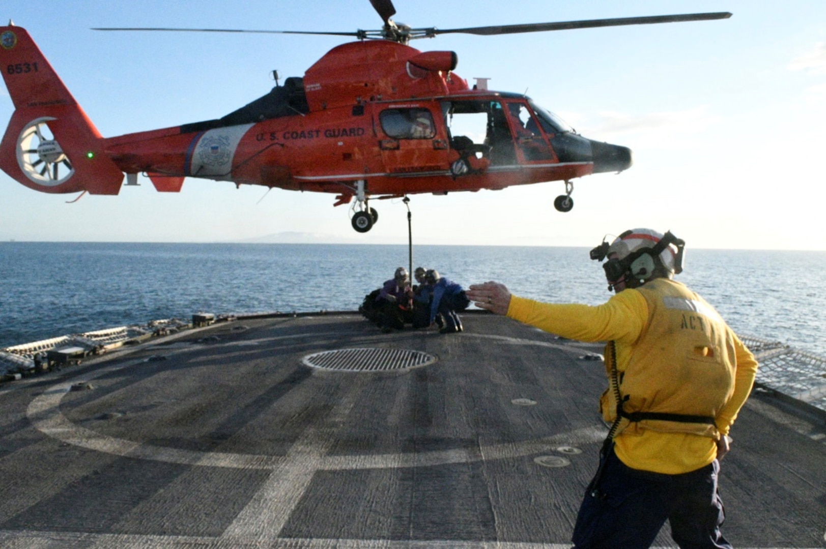 USCGC Active (WMEC 618) landing signal officer Petty Officer 1st Class Ryan Cody directs flight deck personnel during a vertical replenishment (VERTREP) exercise off the coast of Southern California with an MH-65E helicopter aircrew from Forward Operation Base Point Mugu, California, Mar. 17, 2024. A VERTREP is a logistical operation to resupply ships at sea utilizing helicopters to transport supplies and equipment between ships. U.S. Coast Guard photo by Chief Petty Officer Shane Sexton.