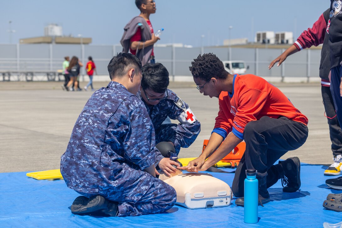 Members of the Japan Maritime Self-Defense Force teach life saving techniques to a student from Marine Corps Air Station Iwakuni during a Science, Technology, Engineering and Mathematics (STEM) day at MCAS Iwakuni, Japan, May 3, 2024.  U.S. Marines, Sailors, and civilians along with Japan Maritime Self-Defense Force members displayed equipment and held interactive demonstrations to teach children about STEM-related careers. (U.S. Marine Corps photo by Cpl. Calah Thompson)