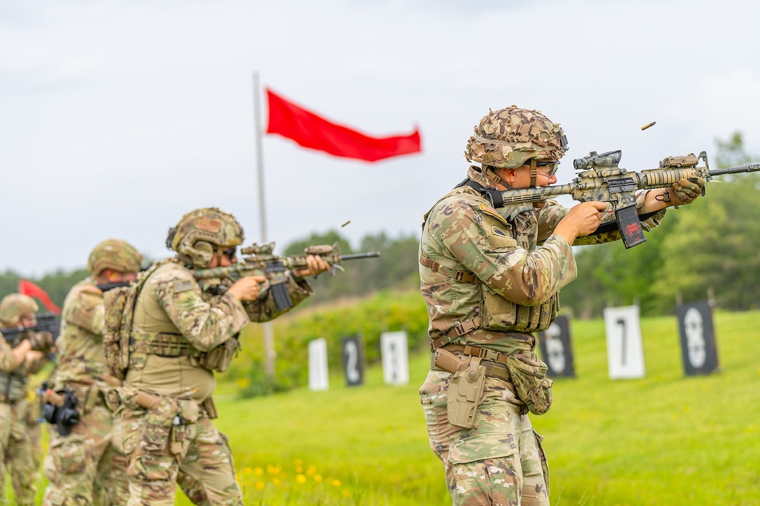 Four service members fire weapons toward targets outdoors during a marksmanship competition.