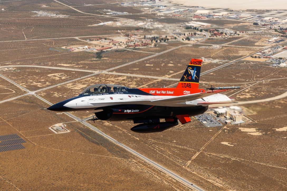 An Air Force aircraft flies over a desert landscape during daylight.