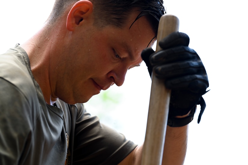 Close-up of a sweaty person leaning against the pole of a garden instrument.