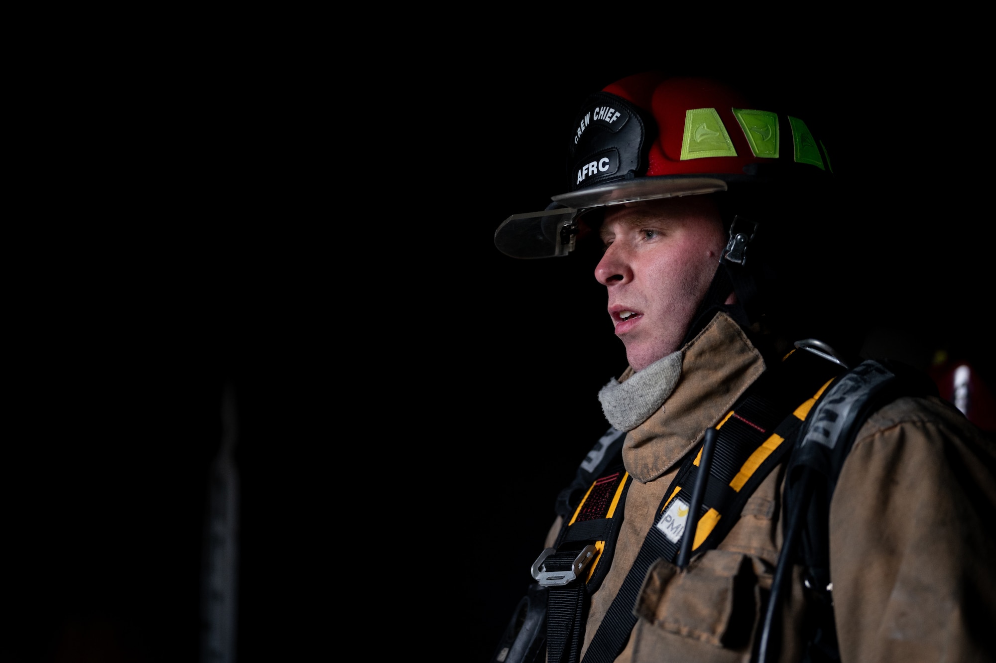 A uniformed firefighter looking to the left of the frame. Only he is visible, the background is all black.