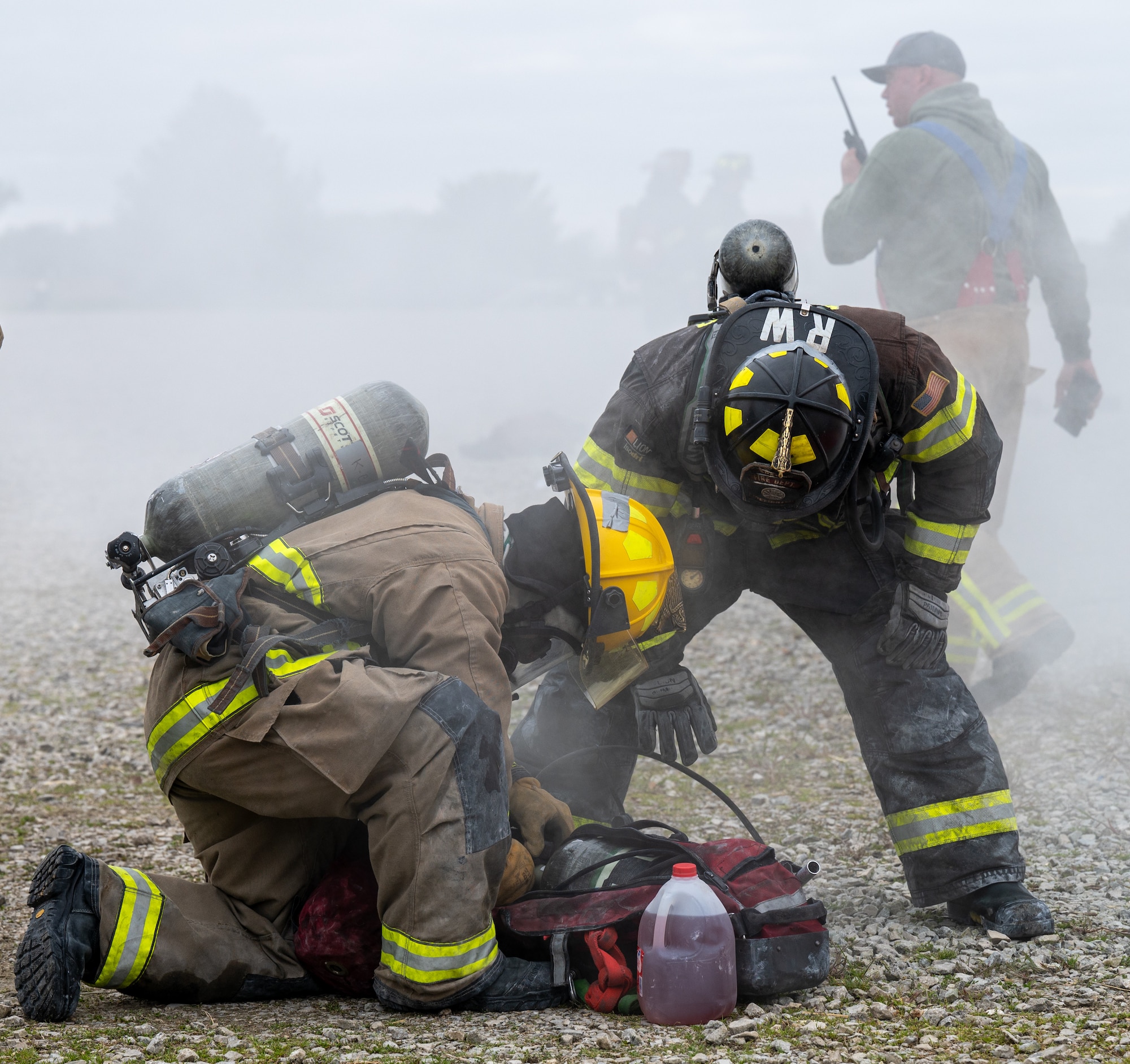 Two firefighters hover over a red bag.