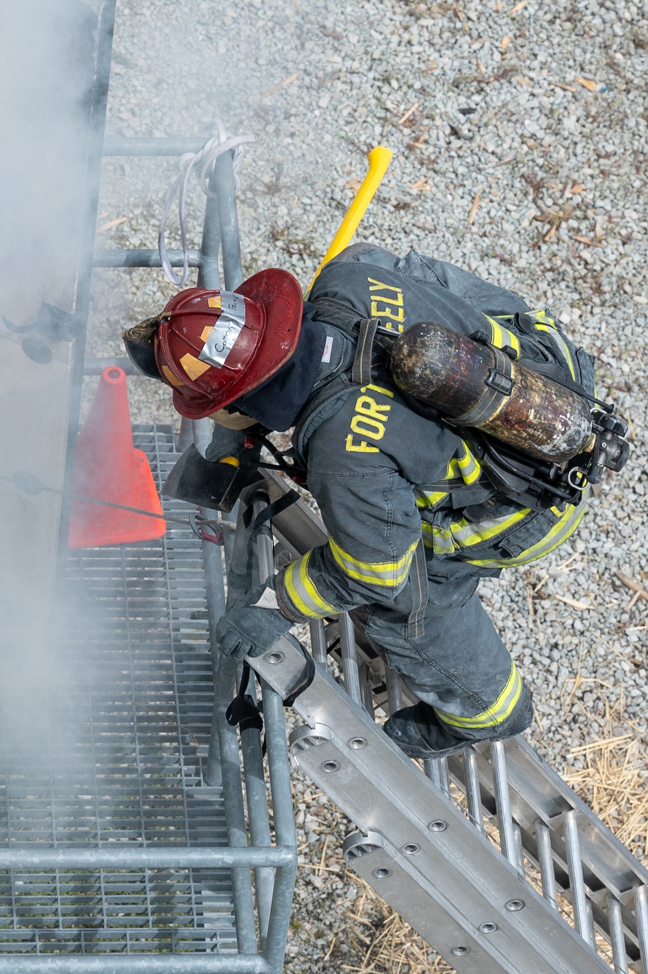 An aerial image of a uniformed firefighter climbing a metal ladder with an axe.