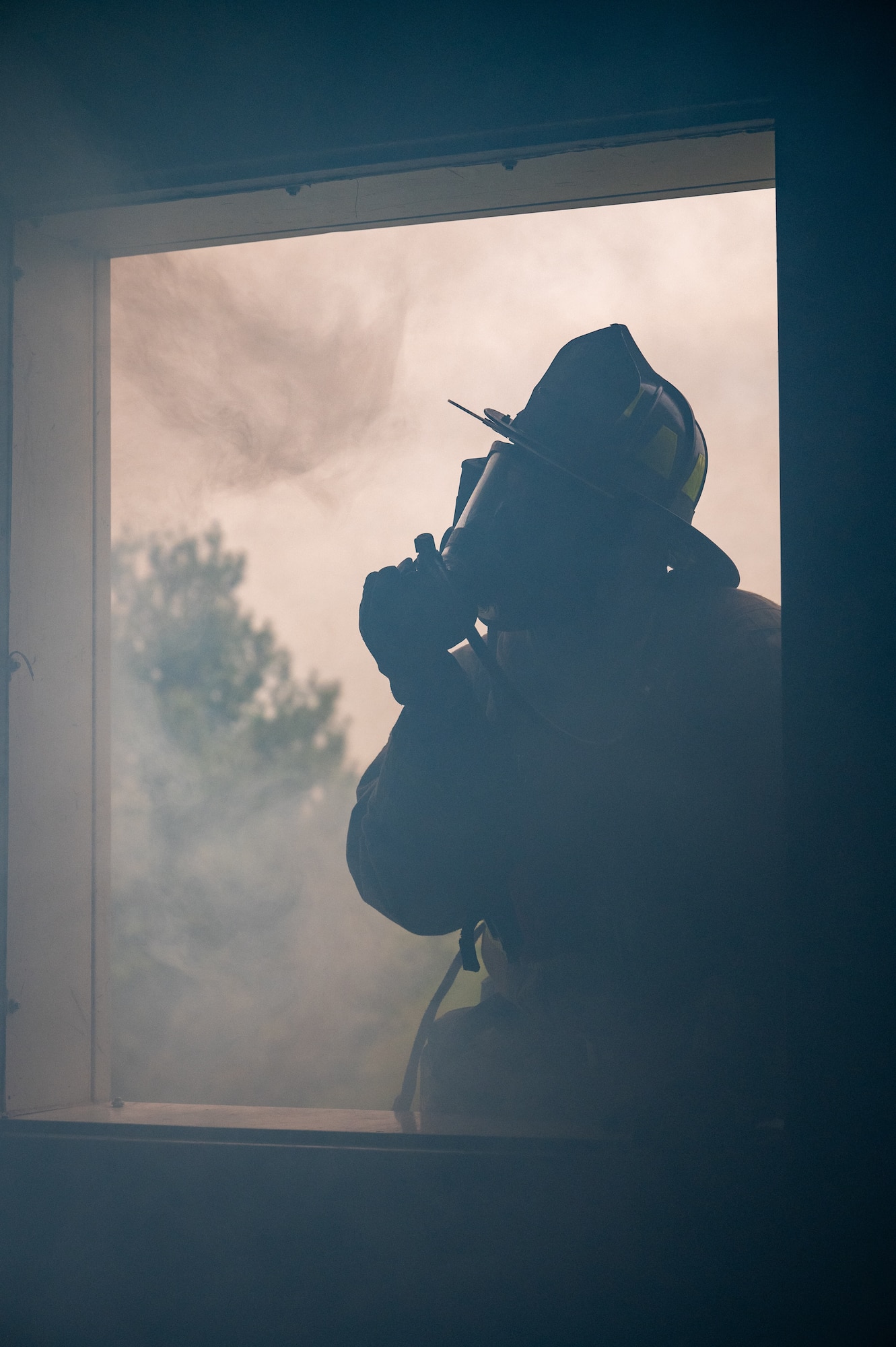 A silhouette of a firefighter is visible in a framed window filling with smoke. The firefighter can be seen adjusting their mask.