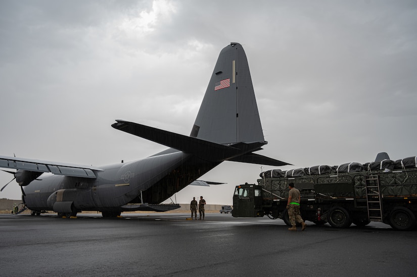 Service members in uniform load pallets of humanitarian aid onto a military cargo plane.