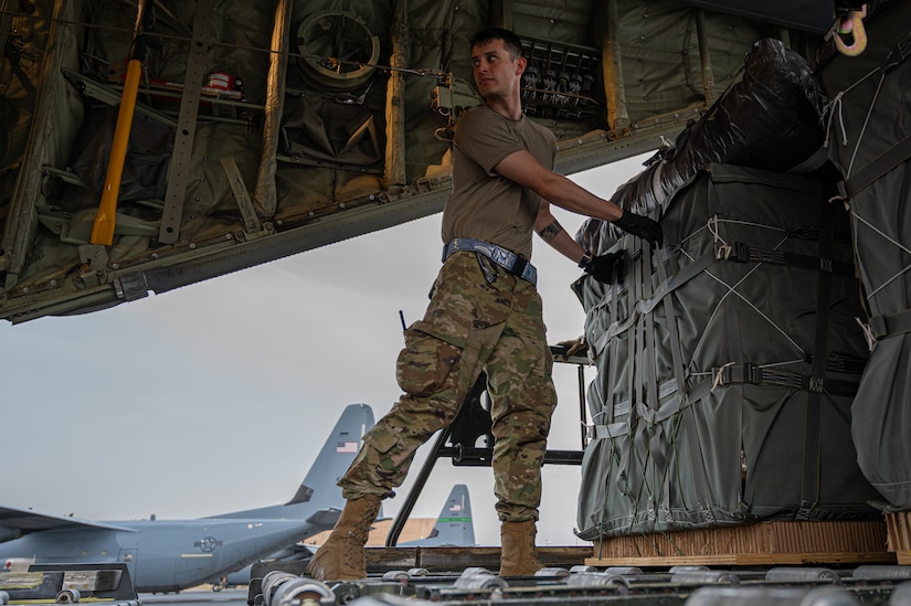 A service member in uniform handles a pallet of humanitarian aid onboard a military cargo plane.