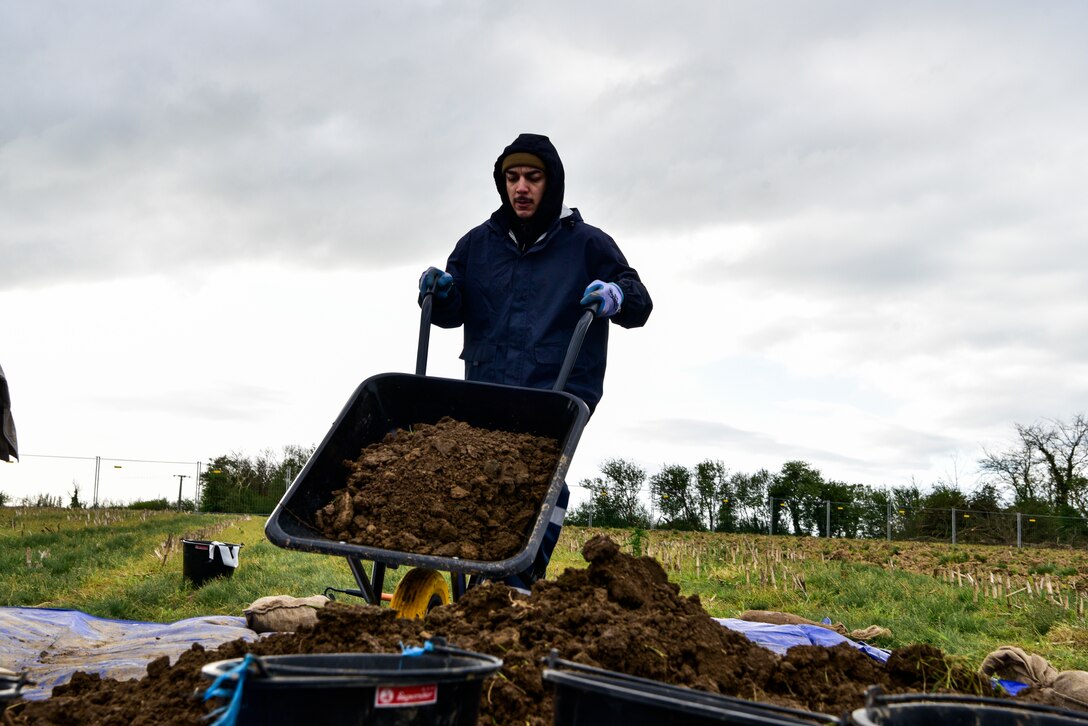 A man dumps a wheelbarrow full of dirt into a pile.