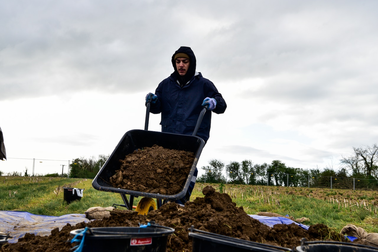 A man dumps a wheelbarrow full of dirt into a pile.
