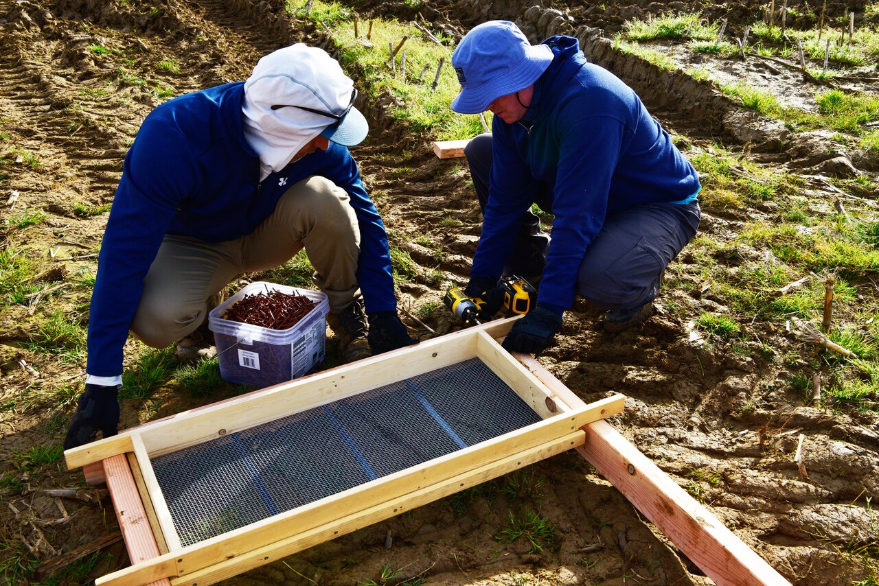 Two men build a dirt sifting station.