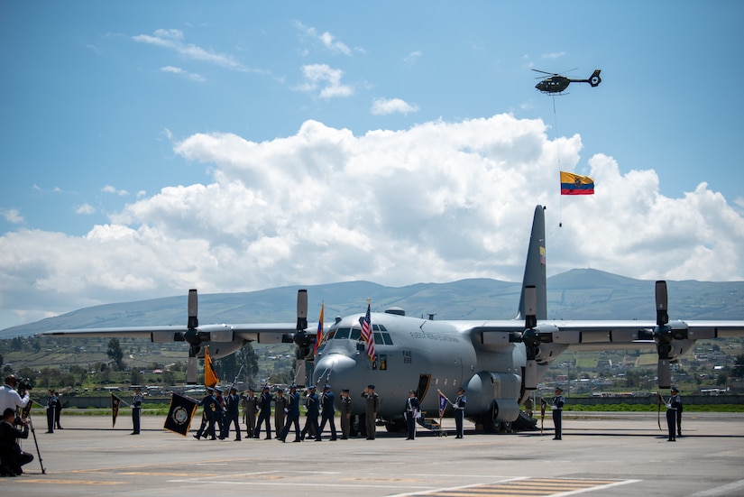 A helicopter flies the Ecuadorian flag above a ceremony welcoming the arrival of a C-130H Hercules to the Ecuadorian Air Force in Latacunga, Ecuador, March 25, 2024. The ceremony, which included top Ecuadorian military and civilian leaders, marked a new milestone in Ecuador’s participation in the National Guard Bureau State Partnership Program, which has paired Ecuador and the Kentucky National Guard for mutual military cooperation. (U.S. Air National Guard photo by Phil Speck)
