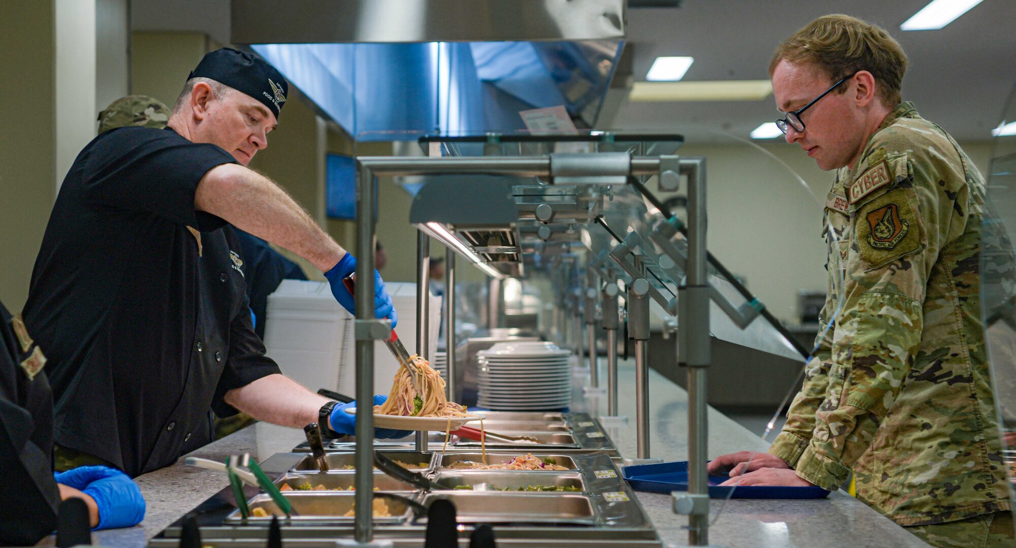 U.S. Air Force Col. John McFarlane 18th Medical Group commander, serves food to an Airman at the Marshall DFAC to celebrate its reopening.