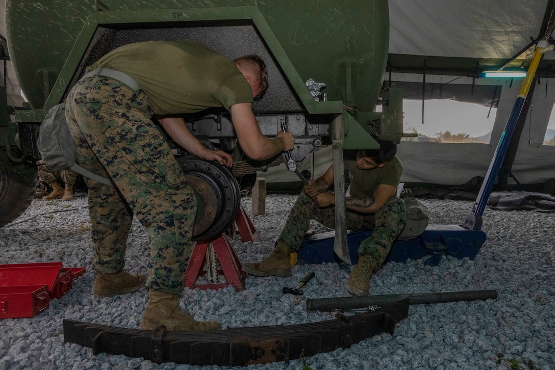 U.S. Marine Corps Lance Cpl. Jaime Barrera, right, and Lance Cpl. Tristin Wigton, left, both automotive maintenance technicians with Regional Maintenance Operations Component North, 3rd Maintenance Battalion, 3rd Marine Logistics Group, remove bolts anchoring a leaf spring on a water trailer during a Marine Corps Combat Readiness Evaluation (MCCRE) at Camp Hansen, Okinawa, Japan, April 17, 2024. Barrera is a native of Texas. Wigton is a native of Minnesota. The purpose of a MCCRE is to formally evaluate the unit's core assigned tasks in order to ensure unit standardization and combat readiness. (U.S. Marine Corps photo by Lance Cpl. Aaliyah Hunt)