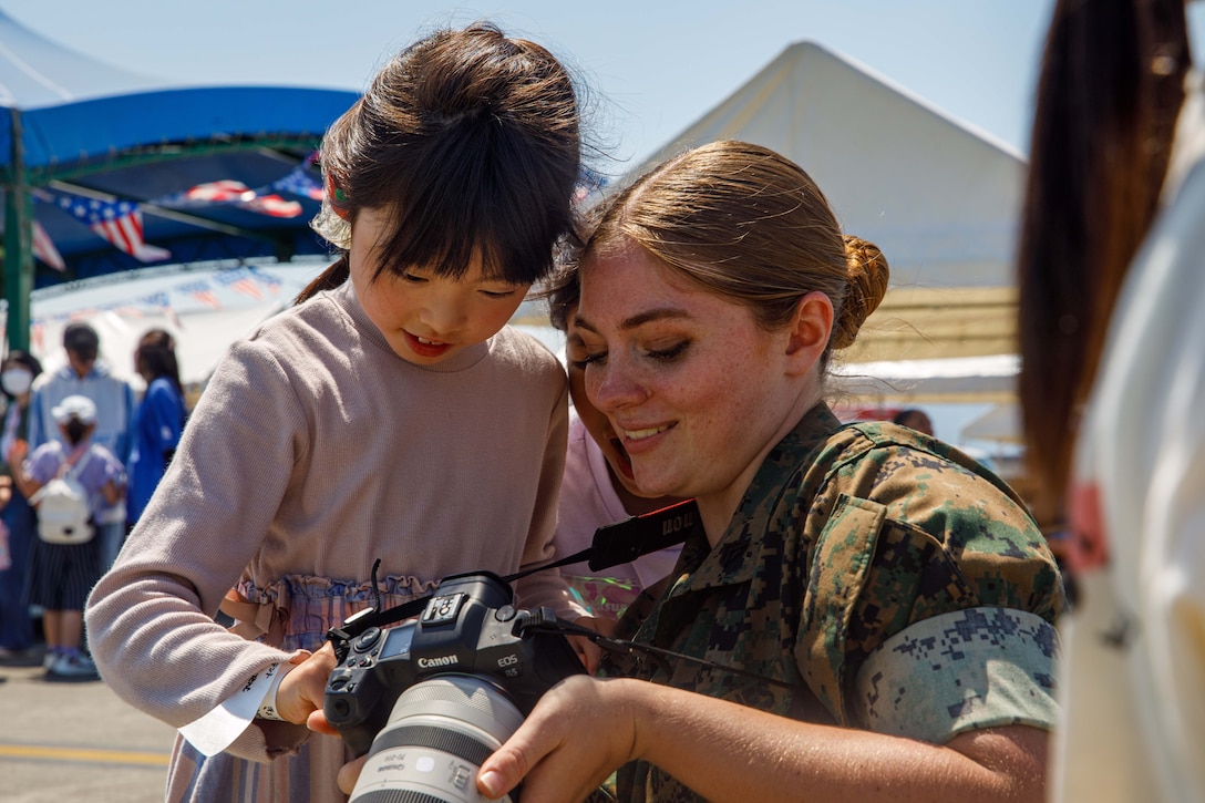 A Marine kneels and shows a child pictures in a camera.