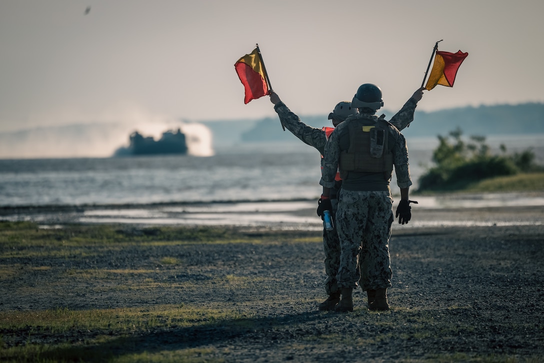 U.S. Navy Sailors wave down a Landing Craft Air Cushion as it approaches a beach during the Annual Amphibious Mobility Exercise at Marine Corps Air Facility on Marine Corps Base Quantico, Virginia, May, 3, 2024. The LCAC is a class of air-cushioned landing craft used by the Navy to transport weapons systems, equipment, cargo and personnel from ship to shore and across the beach. (U.S. Marine Corps photo by Lance Cpl. Ethan Miller)