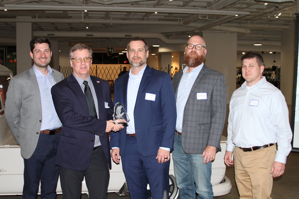Five men stand side by side and the man on the second from the left holds a glass award.