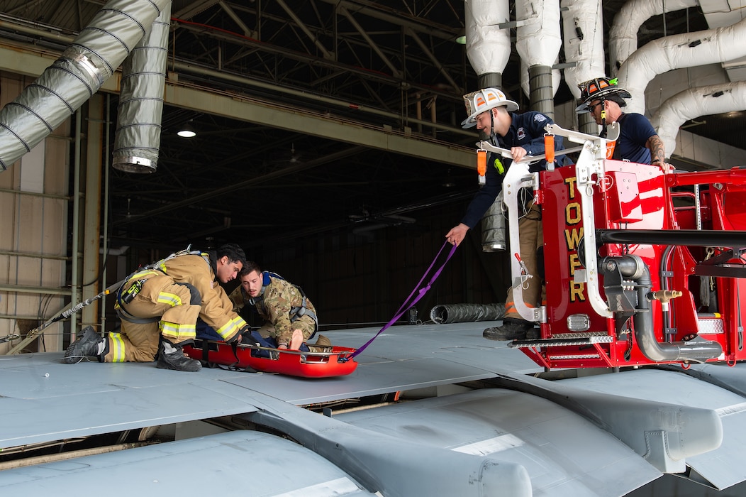 U.S. Air Force Airman 1st Class Brian Castro, far left, 436th Civil Engineer Squadron fire department firefighter, and Senior Airman Matthew Maier, second left, 436th CES fire department driver operator, secure a mannequin in a Stokes basket during a joint simulated rescue at Dover Air Force Base, Delaware, May 3, 2024. Dover AFB first responders and the Dover Fire Department participated in an annual confined-space extraction exercise of a mannequin overcome by simulated fuel vapors on top of the left wing of a C-5M Super Galaxy. (U.S. Air Force photo by Roland Balik)