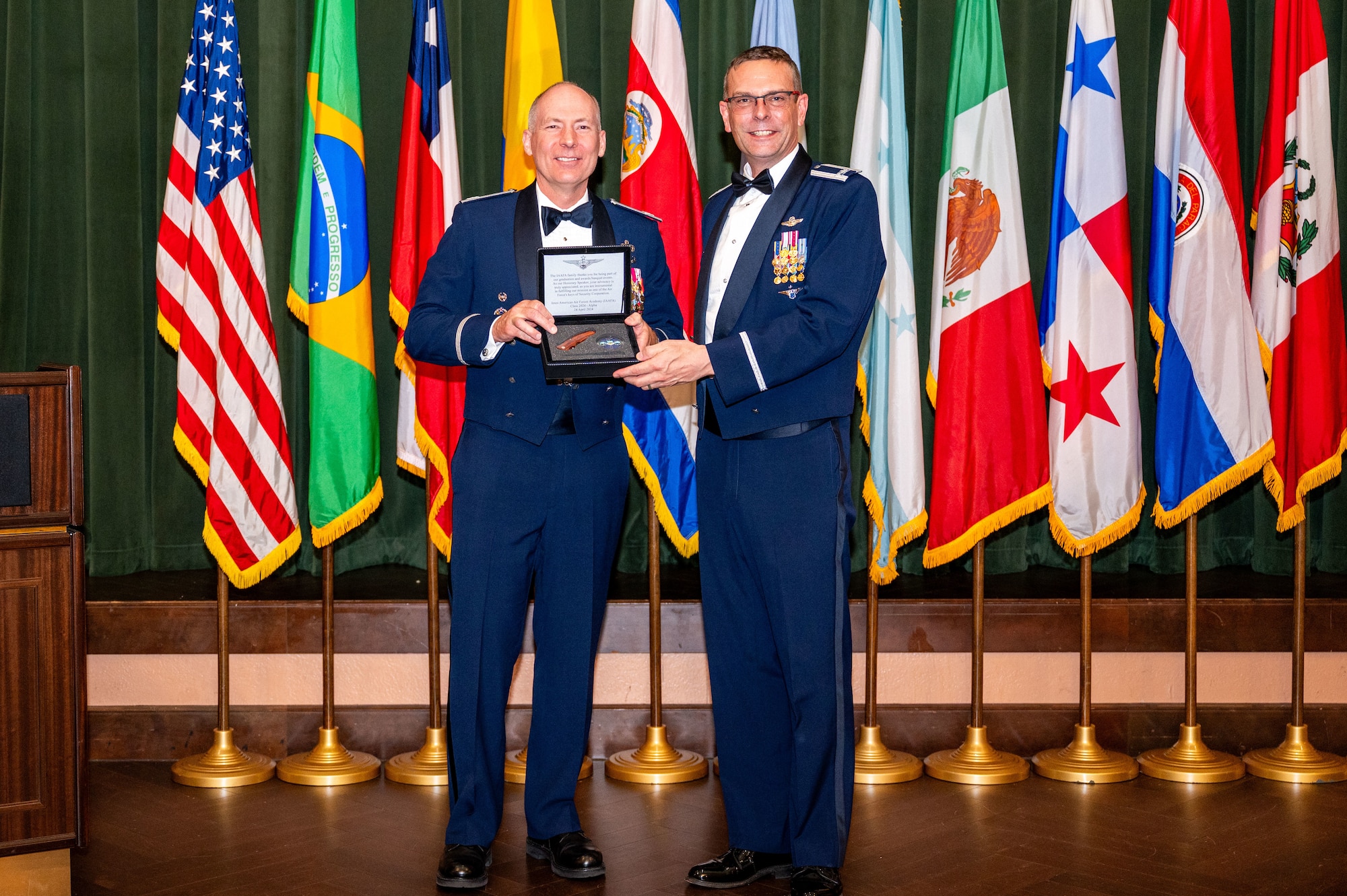 Col. Christopher Callis, Director of Plans, Requirements, Programs and Assessments Directorate from 12th Air Force, accepts a gift of appreciation from Col. Bryan Tuinman, commandant of the Inter-American Air Forces Academy at Joint Base San Antonio-Lackland Texas, April 24, 2024. Callis served as guest of honor for IAAFA’s Alpha-Cycle graduation banquet. Approximately 90 international military students from six partner nations and the U.S. Air Force graduated during the training cycle. IAAFA provides instruction in professional military education and leadership, aircrew training and technical courses – all in Spanish. (U.S. Air Force photo by Vanessa R. Adame)