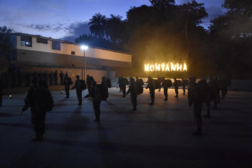 Soldiers gather in front of a building in the dark illuminated by a sign.