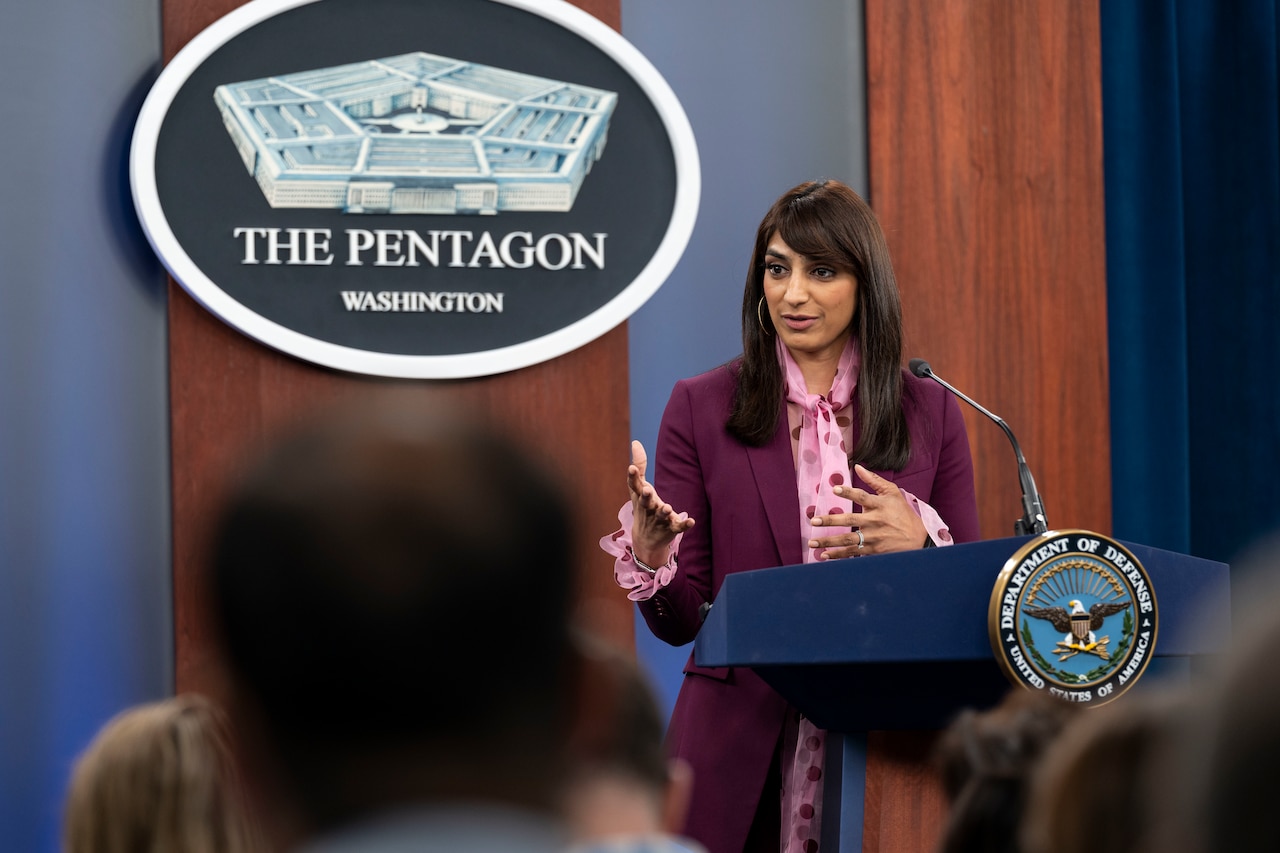 A woman stands behind a lectern. Behind her, a sign says "The Pentagon, Washington."