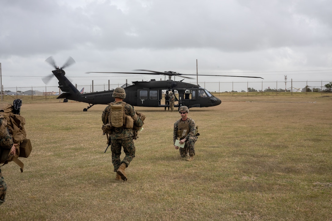 U.S. Marines in the foreground move toward a helicopter in the background.