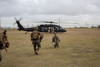 U.S. Marines in the foreground move toward a helicopter in the background.