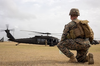 A U.S. Marine kneels in the foreground as he looks toward a helicopter in the background