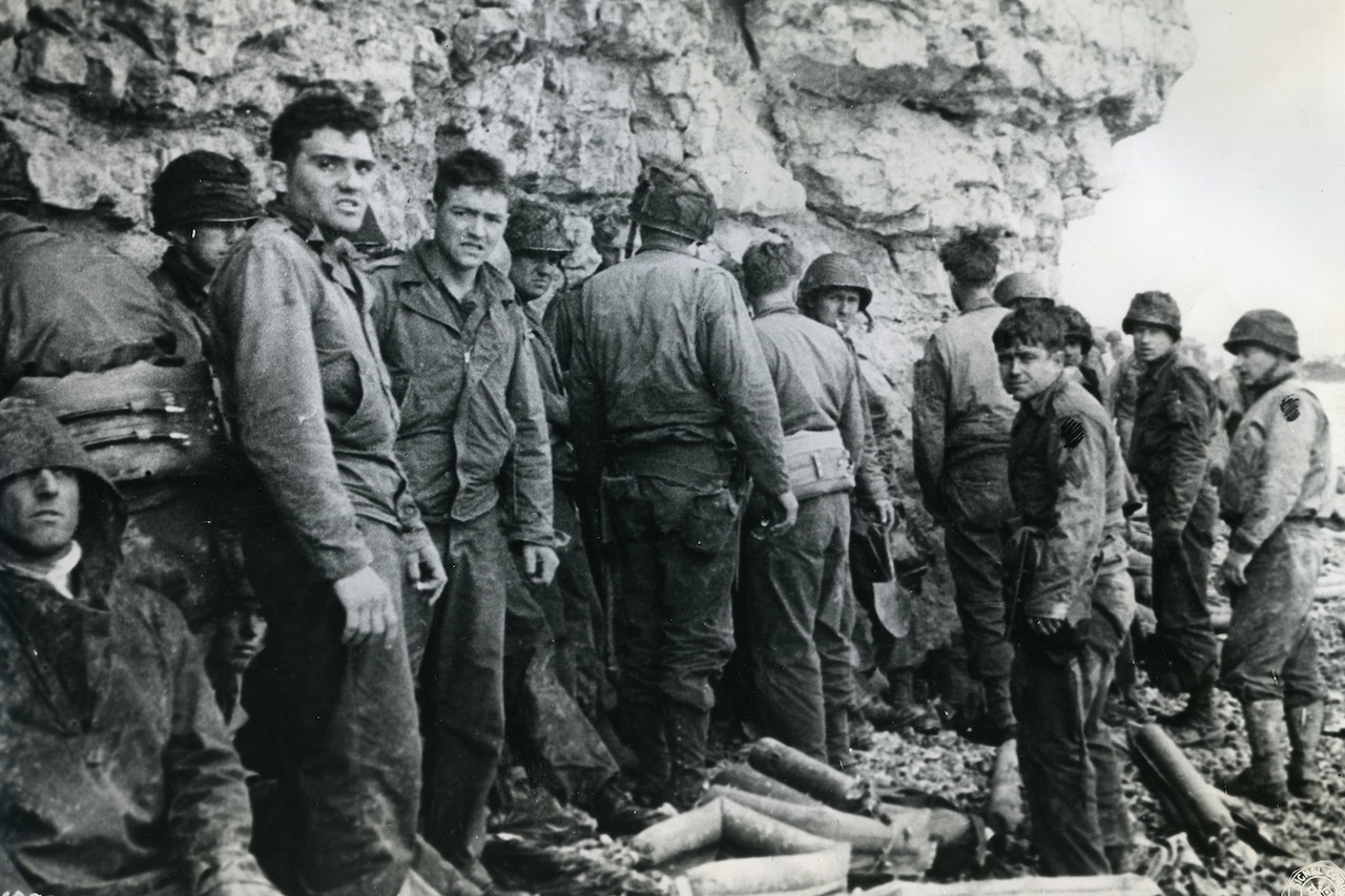 Tired-looking service members stand in the shadow of a cliff.