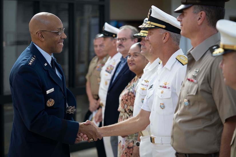 An Air Force officer in uniform shakes hands with a Navy officer in uniform.