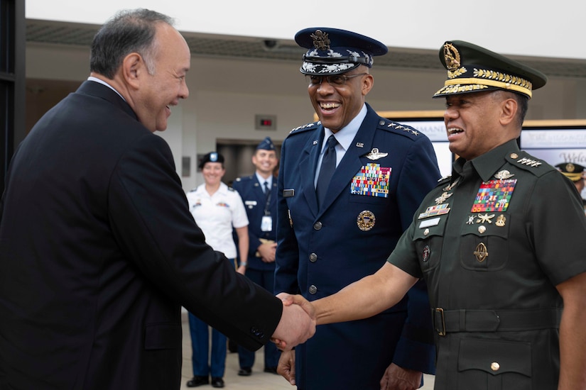 A man in business attire shakes hands with foreign military officer in uniform. An Air Force officer in uniform stands in the midst of the two men.