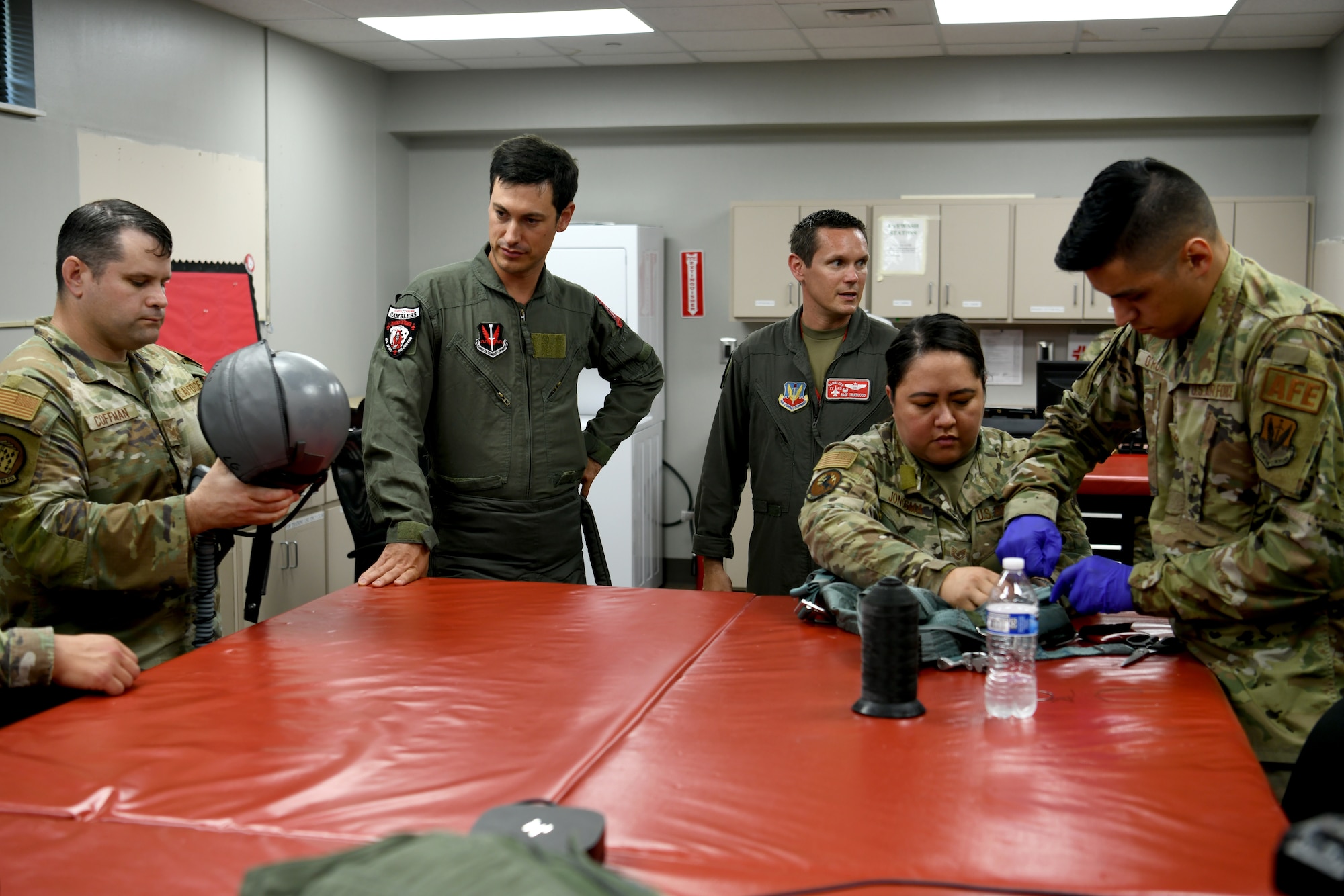 NASCAR driver Joey Logano, second from left, watches while U.S. Air Force 20th Operations Support Squadron Aircrew Flight Equipment technicians prepare his gear prior to flying in an F-16 Fighting Falcon at Shaw Air Force Base, S.C., May 7, 2024. Shaw AFB is dedicated to maintaining a culture and environment of excellence in which everyone can reach their full potential. (U.S. Air Force photo by Staff Sgt. Kelsey Owen)