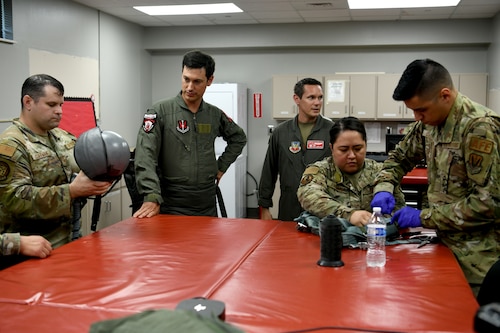 NASCAR driver Joey Logano, second from left, watches while U.S. Air Force 20th Operations Support Squadron Aircrew Flight Equipment technicians prepare his gear prior to flying in an F-16 Fighting Falcon at Shaw Air Force Base, S.C., May 7, 2024. Shaw AFB is dedicated to maintaining a culture and environment of excellence in which everyone can reach their full potential. (U.S. Air Force photo by Staff Sgt. Kelsey Owen)