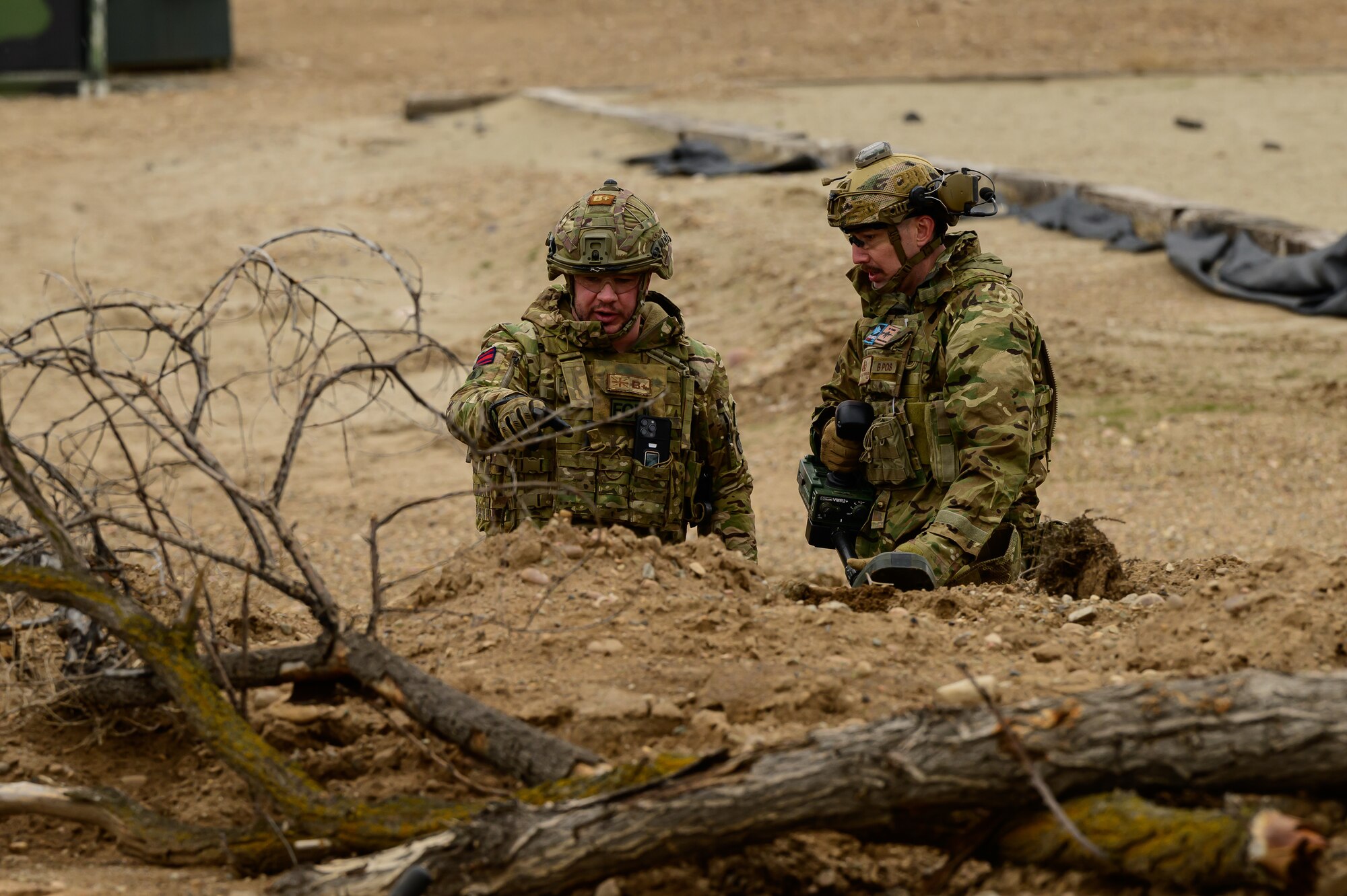 Two me wearing tactical gear discuss operations in a desert setting