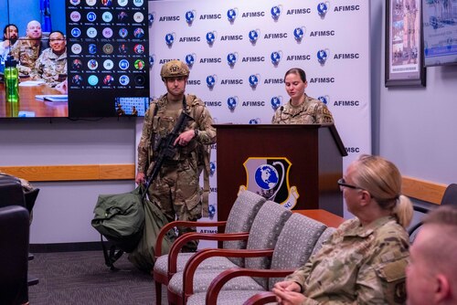 Two Airmen stand in front to present equipment Airmen would wear in a training exercise