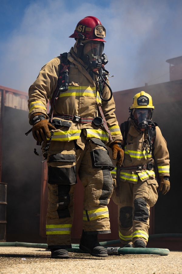 Capt. James Carroll, a Yucca Valley, California native, A-shift captain, left, and Paige Kelly, a Hemet, California native, firefighter, both with The Combat Center Fire Department, Marine Corps Air-Ground Combat Center, exit a building after putting out a controlled fire during routine training at MCAGCC, Twentynine Palms, California, April 22, 2024. The Combat Center Fire Department’s mission is to improve the quality of life at the MCAGCC by providing high quality emergency fire and rescue services, and a fire prevention program.  (U.S. Marine Corps photo by Cpl. Hunter Wagner)