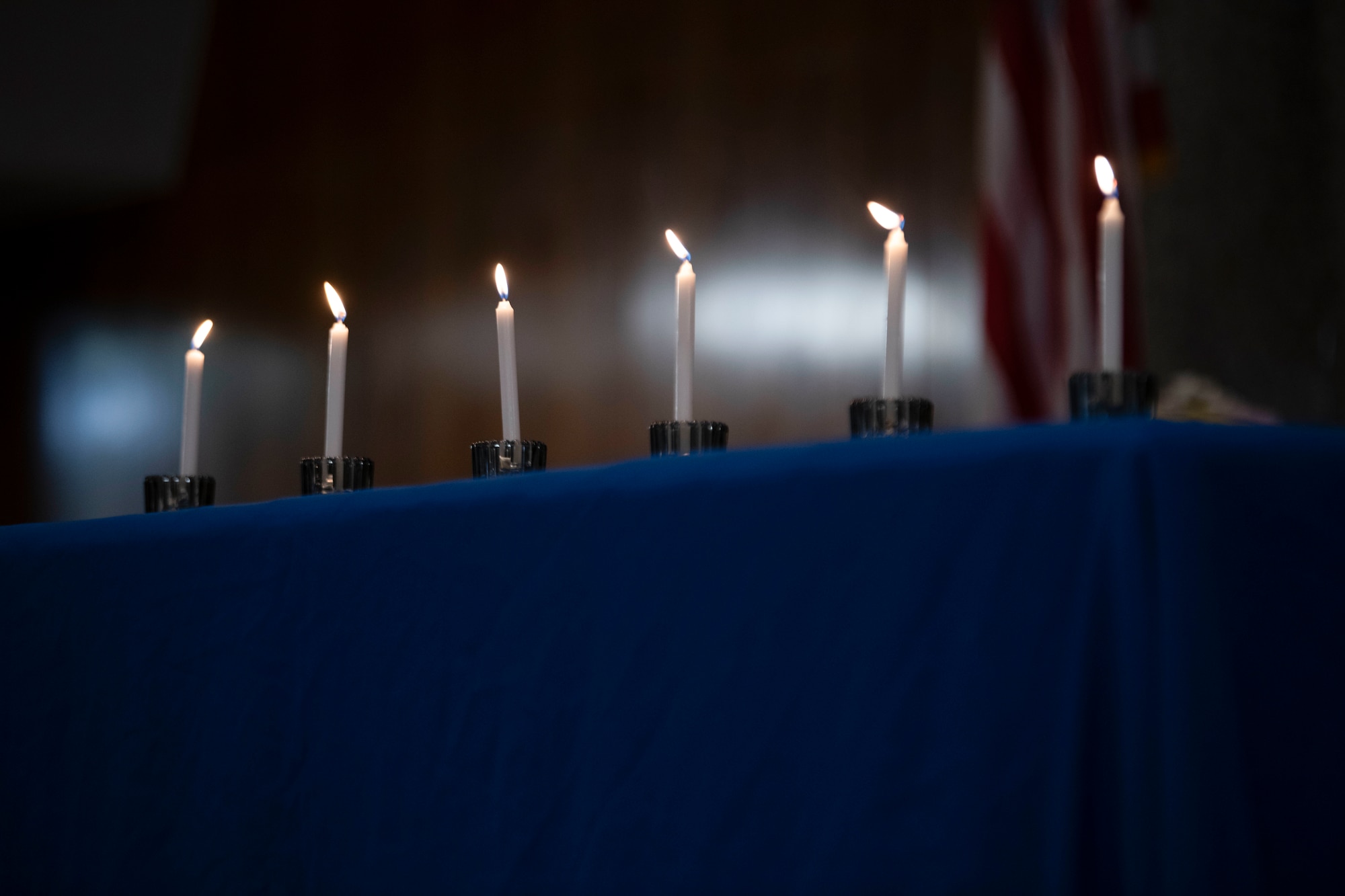 Six lit candles are displayed on a blue tableclothed table.