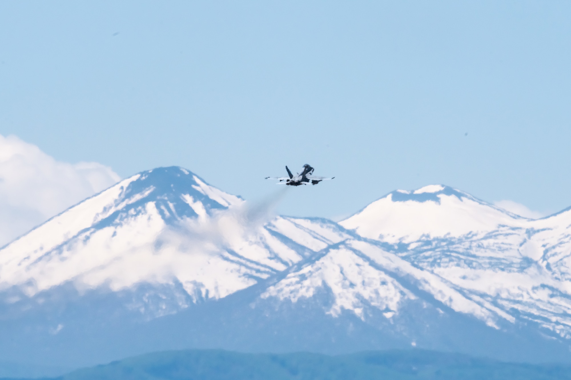 A U.S. Navy fighter jet flies in front of a snow-capped mountain range