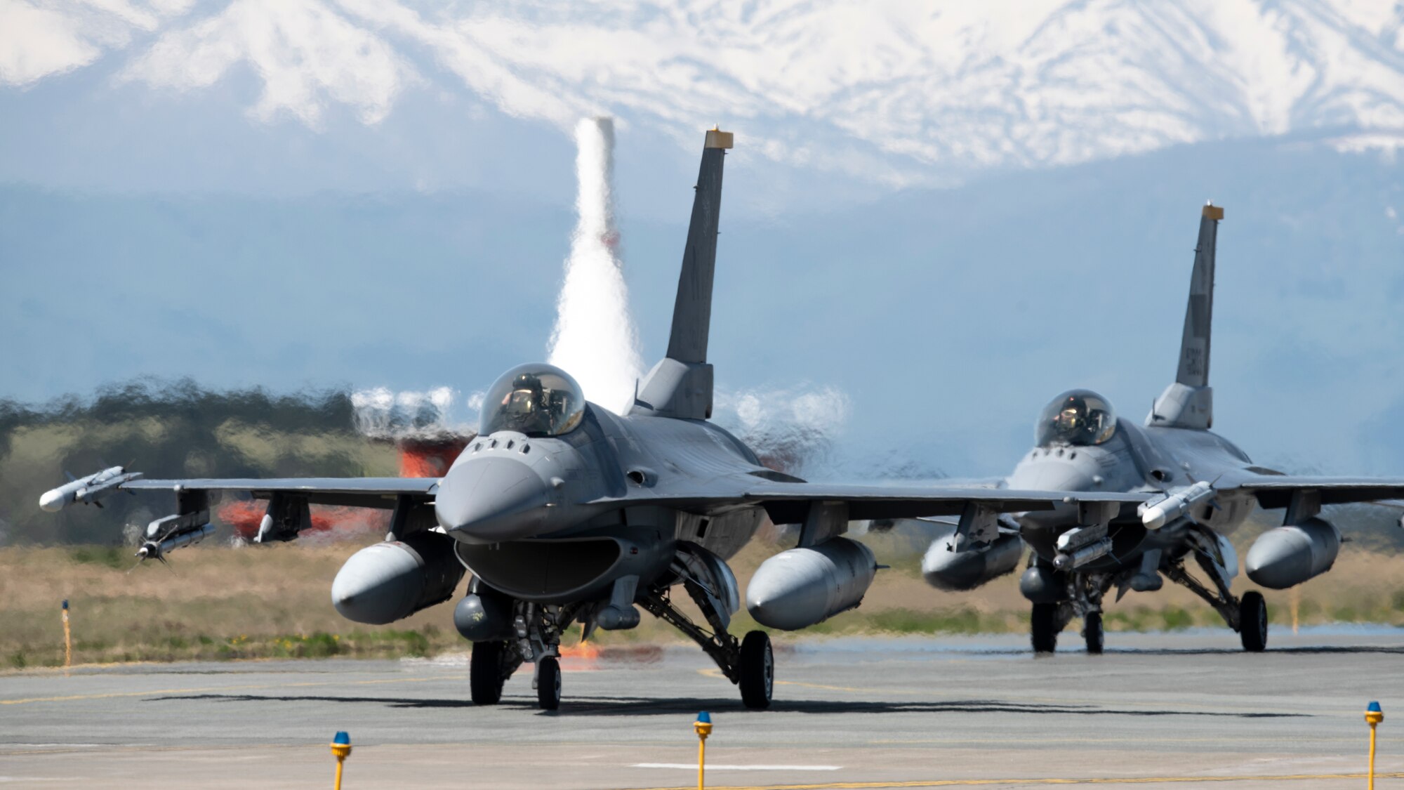 Two F-16 fighter jets taxi down the flightline in front of a mountain range backdrop