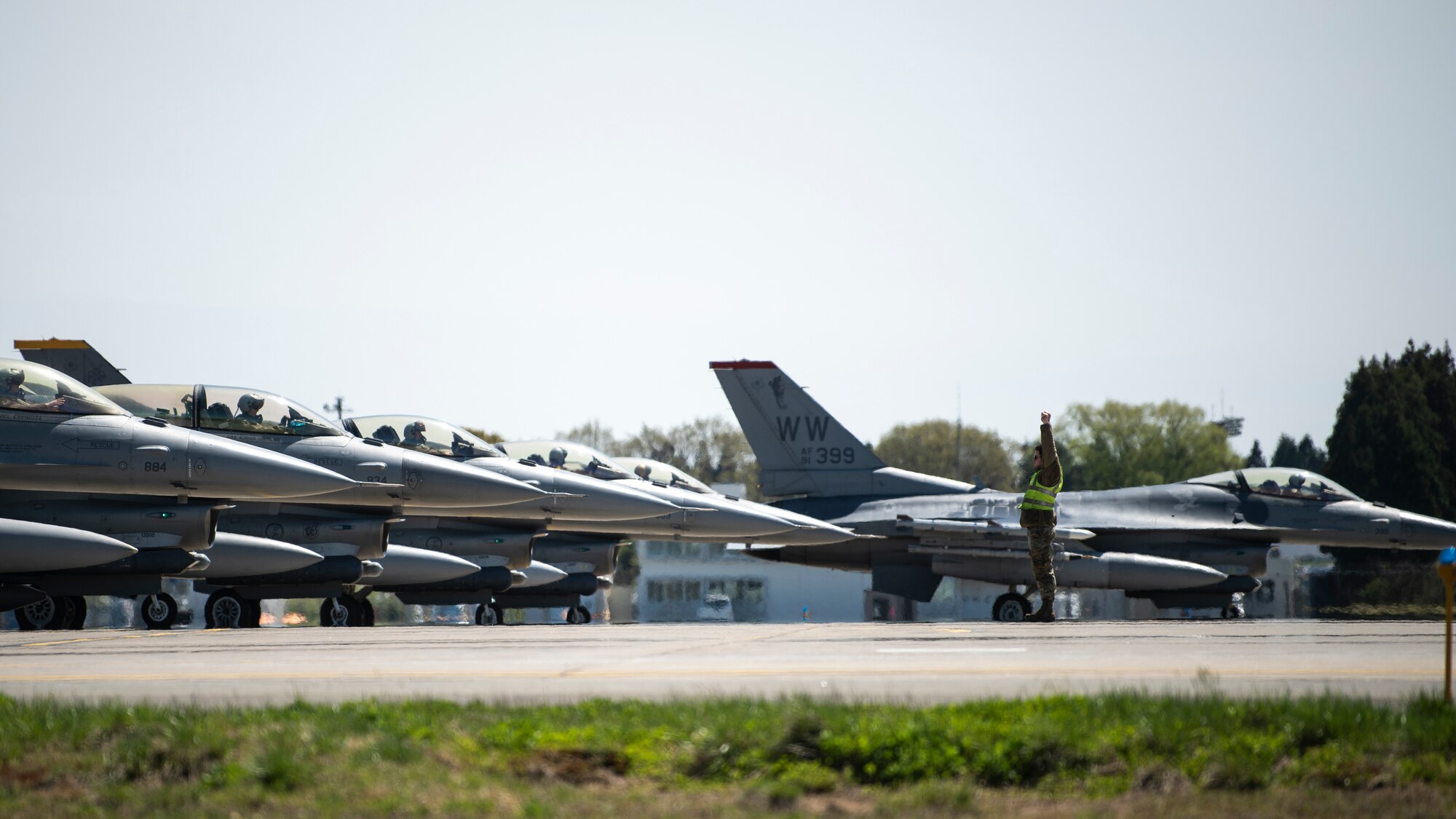 An Airman marshals several F-16 fighter jets on the flightline