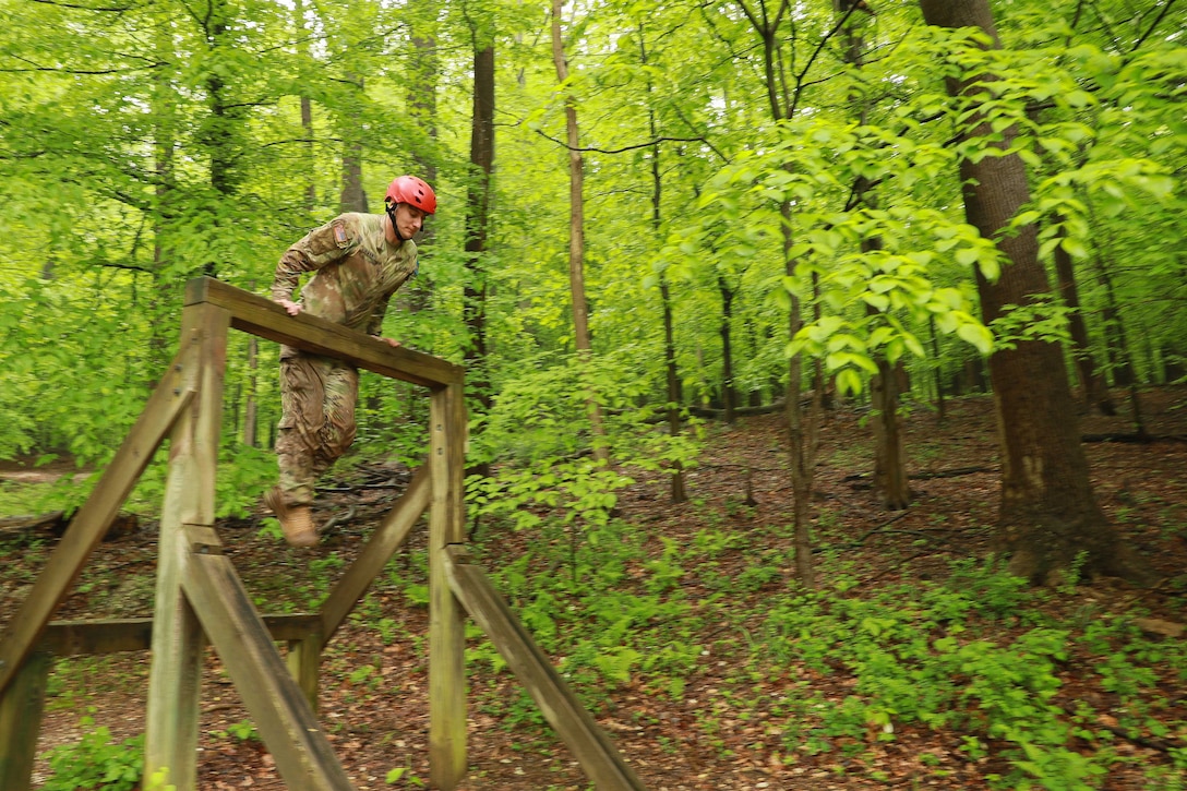 A soldier hoists over the top bar on a wooden obstacle in the woods.