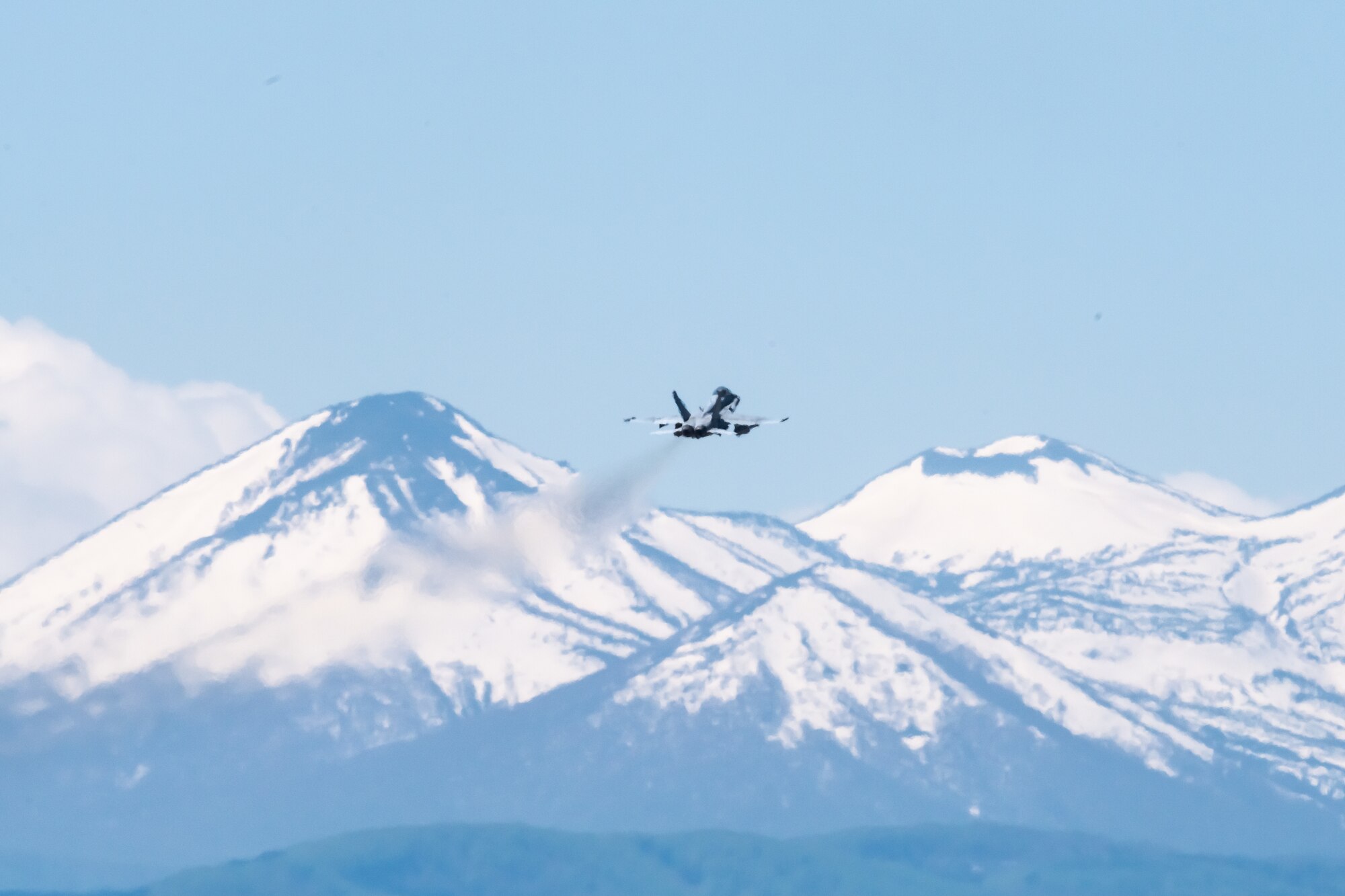 A U.S. Navy fighter jet flies in front of a snow-capped mountain range