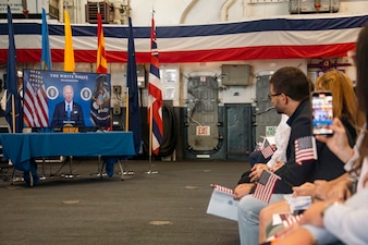 Guests attending a naturalization ceremony aboard USS Bataan (LHD 5) watch a televised message from President Joe Biden during Fleet Week Miami.