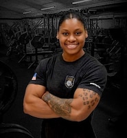 Woman wearing a black t-shirt with a black and white gym display behind her.