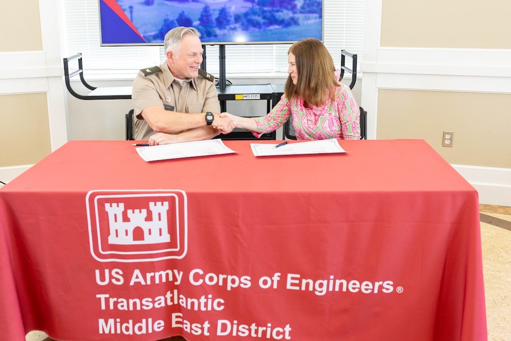 Two people shake hands after signing a document.